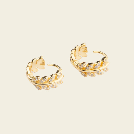 Pair of gold hoop earrings with floral designs on a beige background