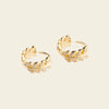 Pair of gold hoop earrings with floral designs on a beige background