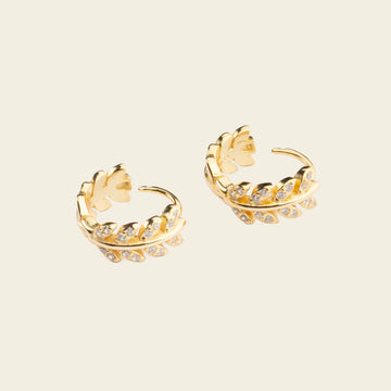 Pair of gold hoop earrings with floral designs on a beige background