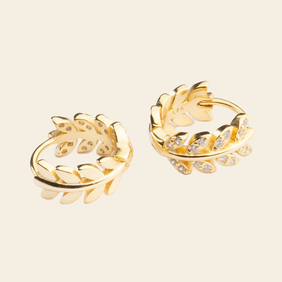 Pair of gold hoop earrings with leaf designs on a beige background