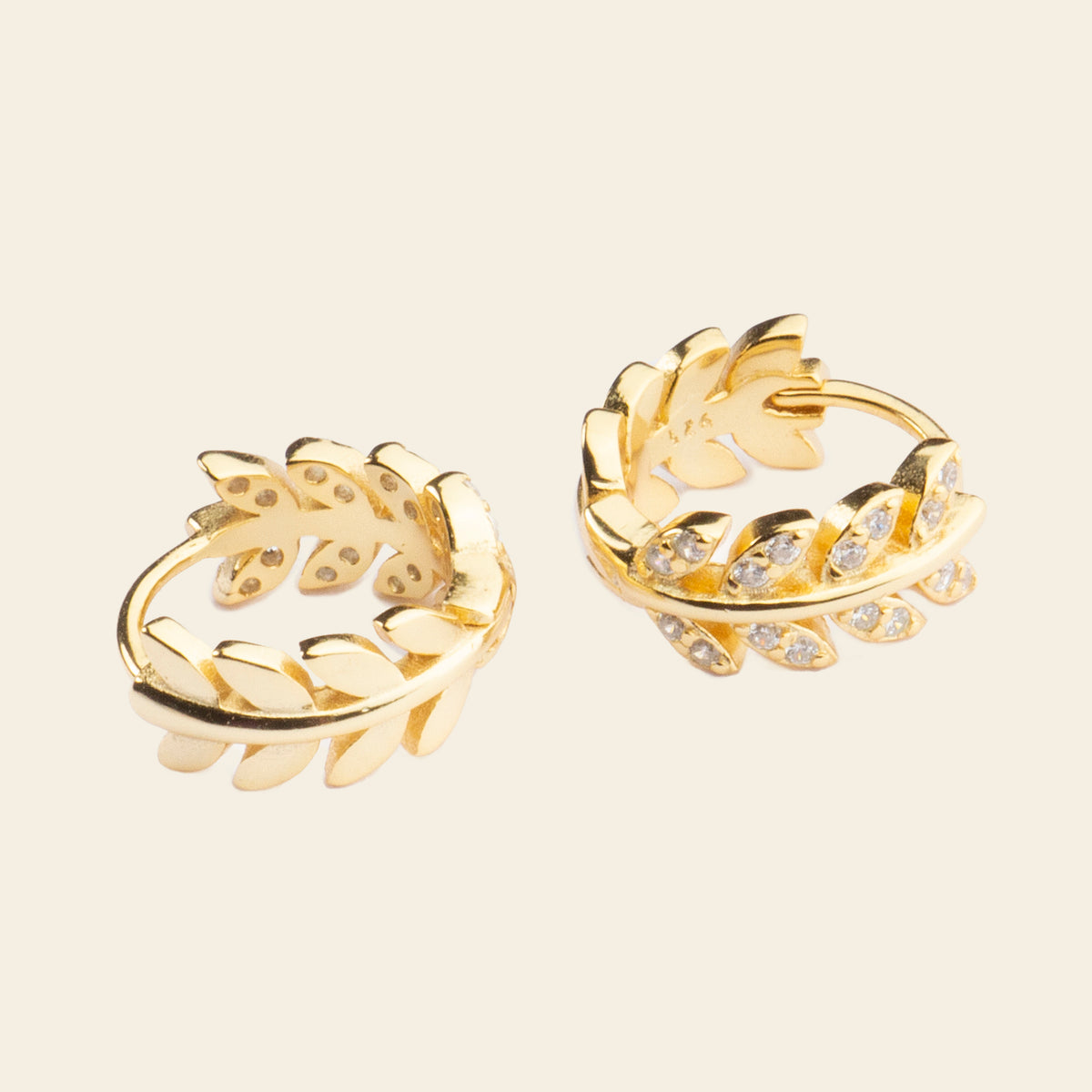 Pair of gold hoop earrings with leaf designs on a beige background