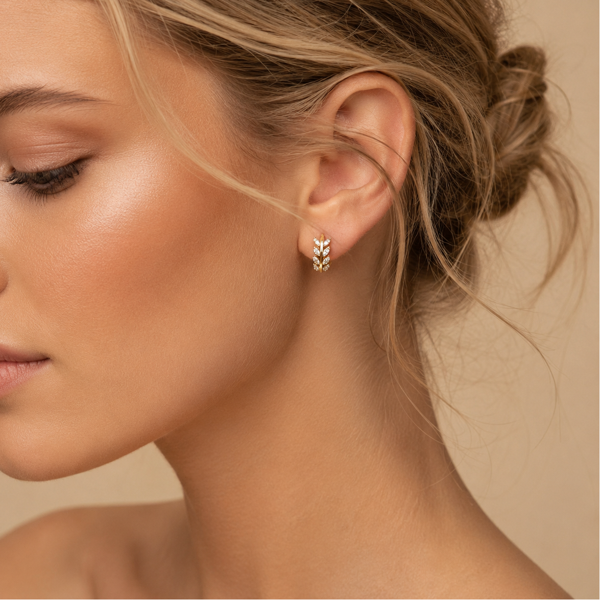 Close-up of a woman wearing gold hoop earrings with a neutral background