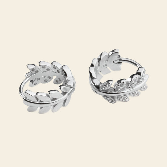 Pair of silver hoop earrings with leaf-like designs on a light beige background