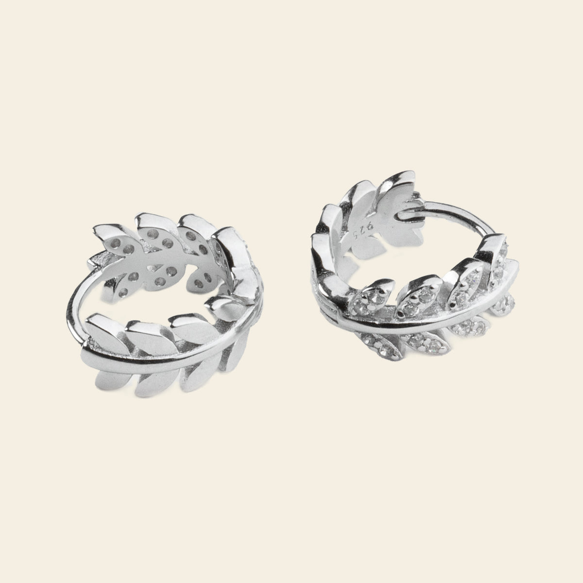 Pair of silver hoop earrings with leaf-like designs on a light beige background