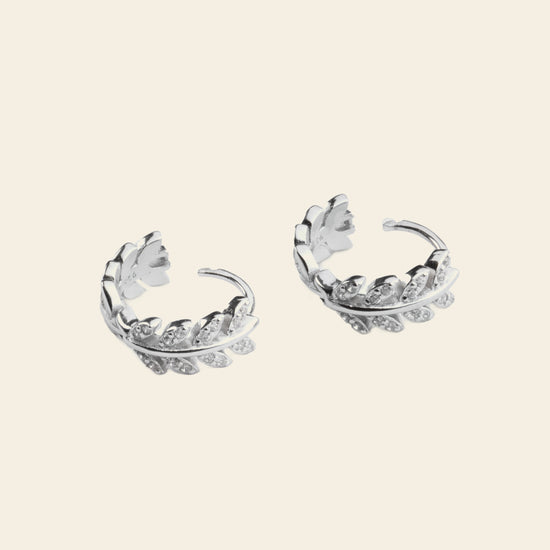 Pair of silver hoop earrings with floral designs on a light beige background