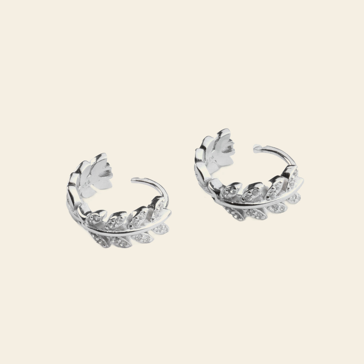 Pair of silver hoop earrings with floral designs on a light beige background