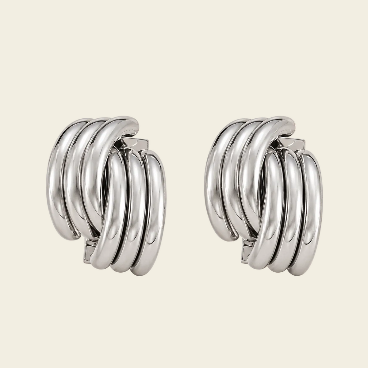 A pair of polished silver hoop earrings with multiple concentric curved bands, displayed on a solid light beige background.