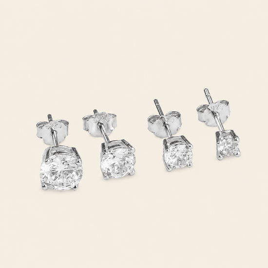 Two pairs of silver stud earrings with large clear square-cut gemstones, shown on a light beige background.