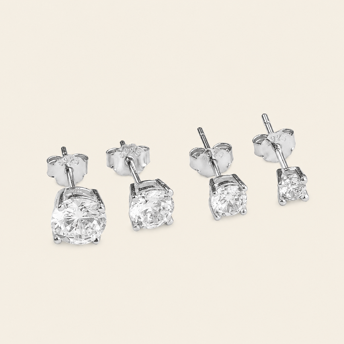 Two pairs of silver stud earrings with large clear square-cut gemstones, shown on a light beige background.