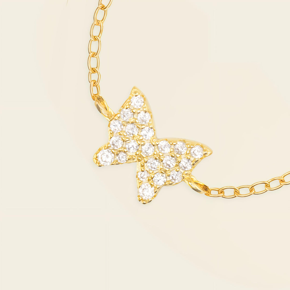 Gold butterfly necklace with clear stones on a beige background