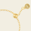 Gold ring with a round gold bead and a tag on a beige background