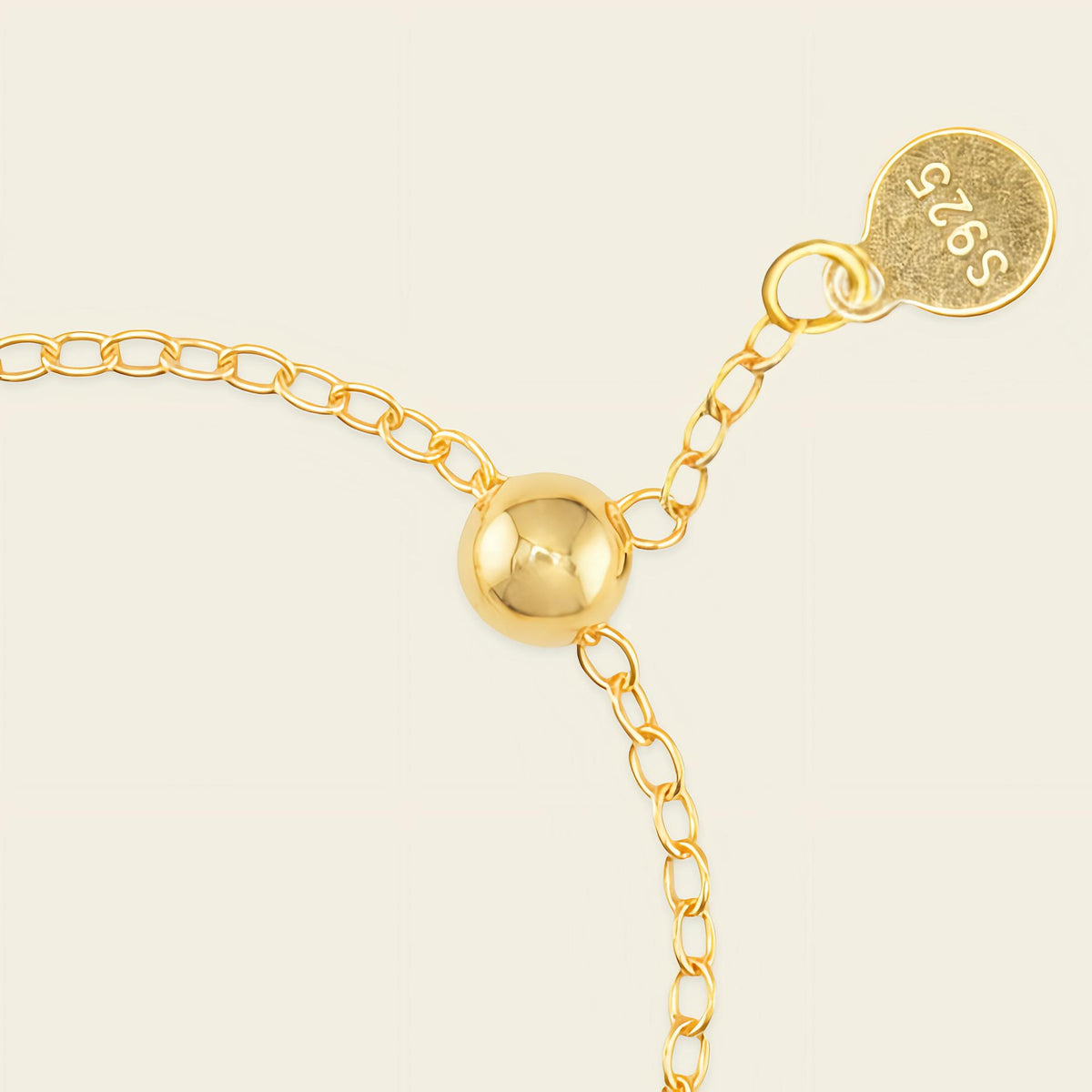 Gold ring with a round gold bead and a tag on a beige background