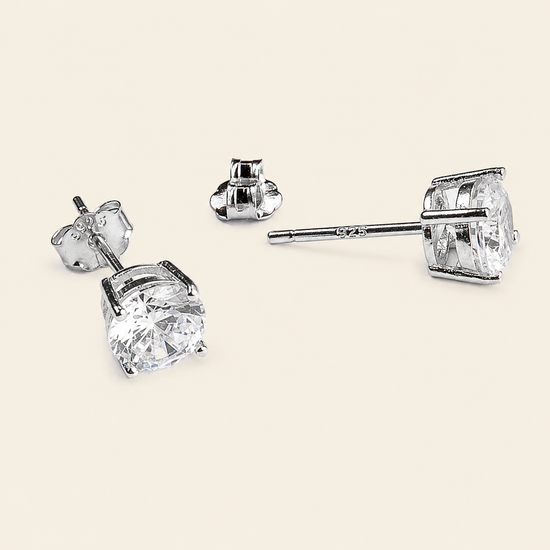 A pair of silver stud earrings with large clear square-cut gemstones, shown from multiple angles on a light beige background.