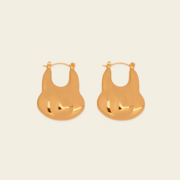 A pair of gold-toned, organic-shaped hoop earrings with a polished, reflective finish, displayed on a solid light beige background.