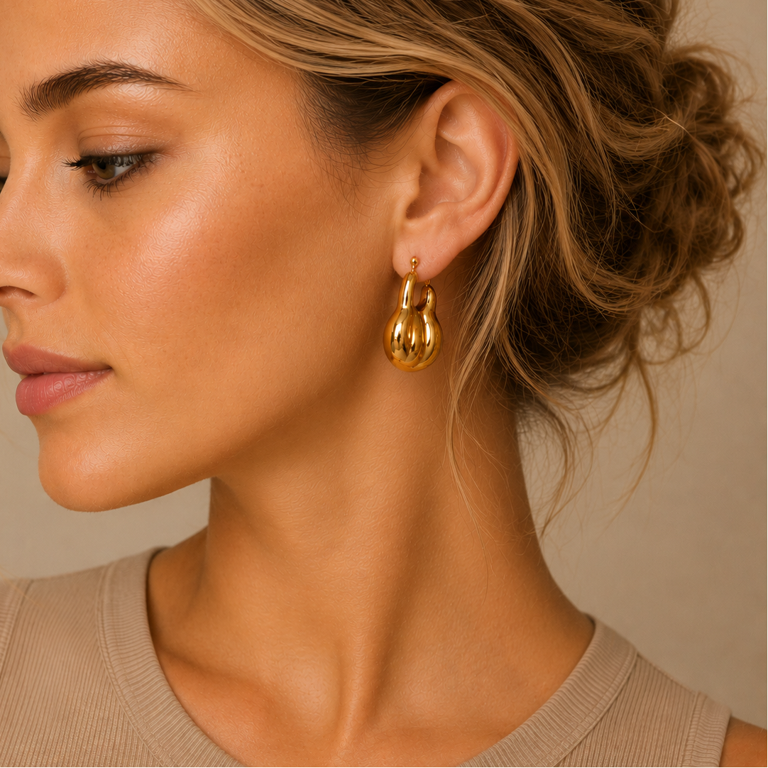 Close-up of a woman wearing gold hoop earrings with a neutral background