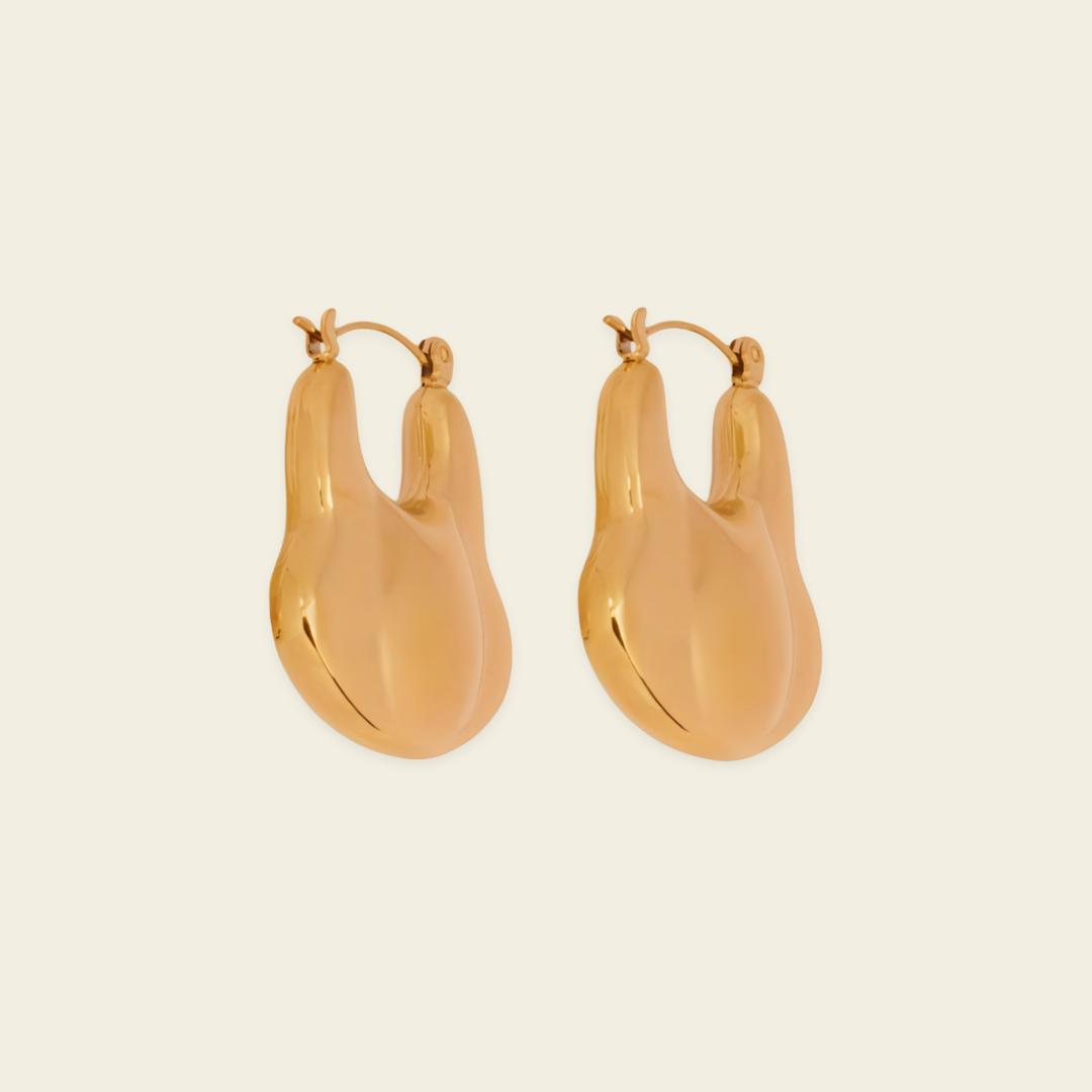 A pair of gold-toned, organic-shaped hoop earrings with a polished finish, displayed on a solid light beige background.