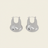A pair of silver-toned, organic-shaped hoop earrings with a polished, reflective finish, displayed on a solid light beige background.