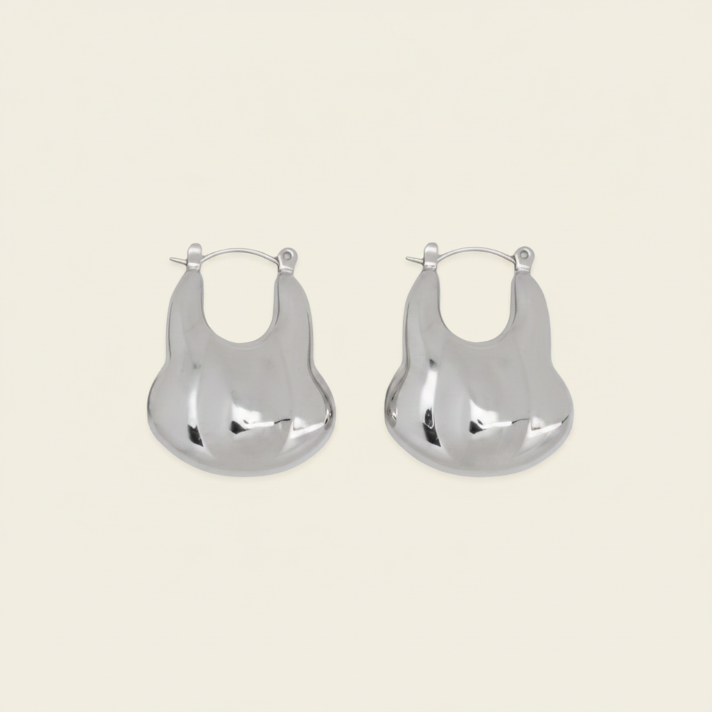 A pair of silver-toned, organic-shaped hoop earrings with a polished, reflective finish, displayed on a solid light beige background.