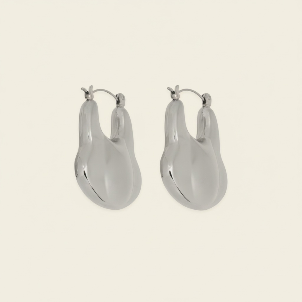 A pair of silver-toned, organic-shaped hoop earrings with a polished finish, displayed on a solid light beige background.