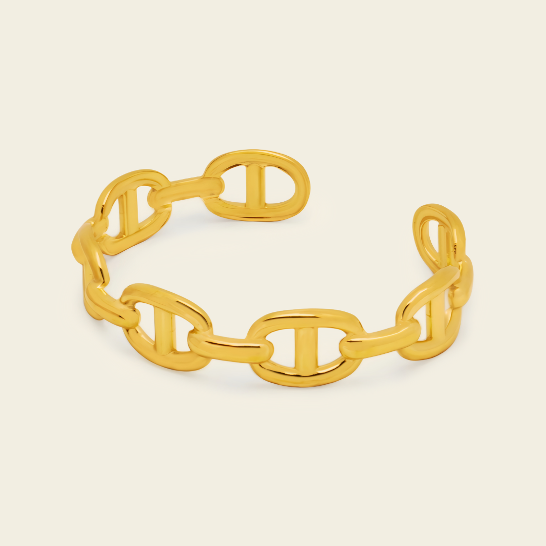 A gold chain-link cuff bracelet with a polished finish, displayed on a light beige background.