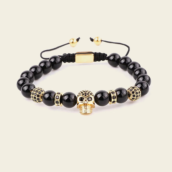 Black beaded bracelet with gold skull charm on a beige background