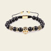 Black beaded bracelet with gold skull charm on a beige background