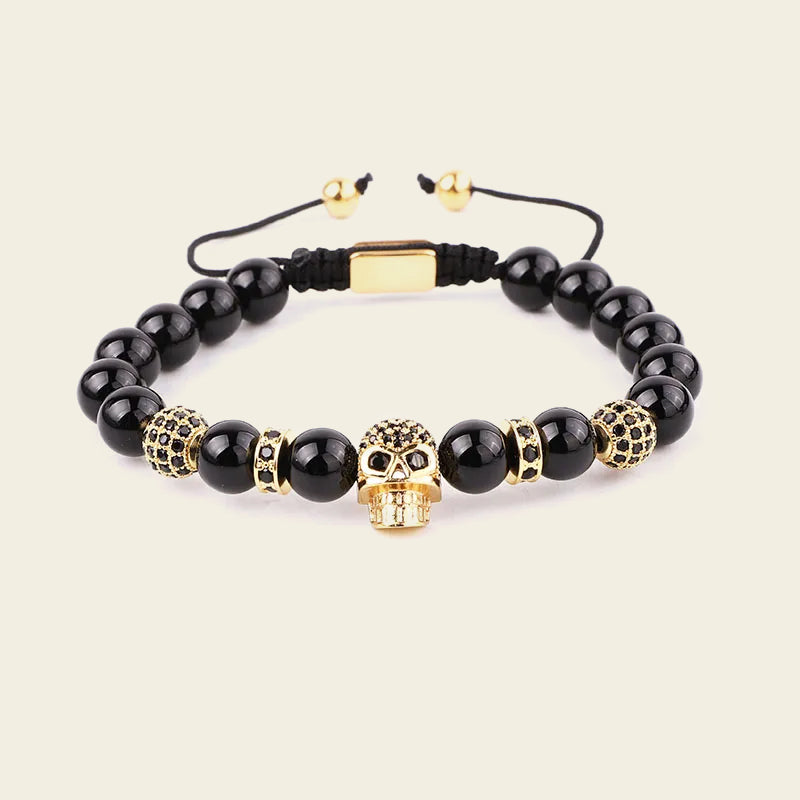 Black beaded bracelet with gold skull charm on a beige background