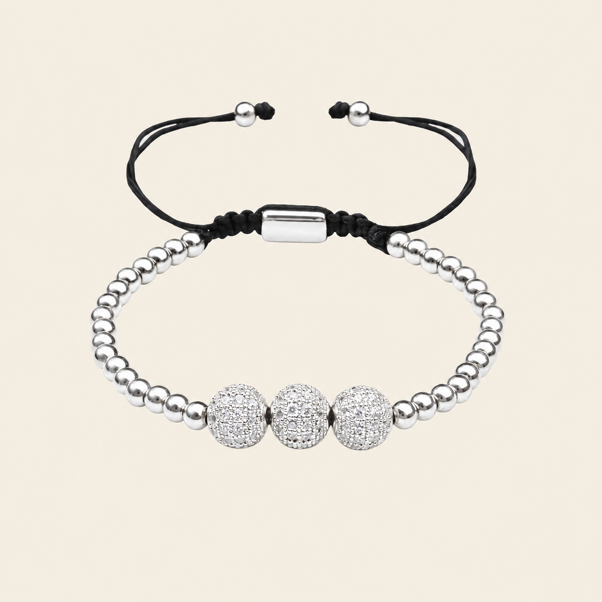 A silver beaded bracelet with three round pavé-style center beads and adjustable black cord ends, shown on a plain warm beige background.