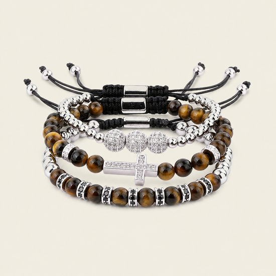 Four beaded stretch bracelets stacked together on a light beige background. The bracelets feature brown tiger's eye beads, silver-toned metal spacers, black cord wraps, and a silver-toned cross charm embellished with clear rhinestones.