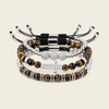 Four beaded stretch bracelets stacked together on a light beige background. The bracelets feature brown tiger's eye beads, silver-toned metal spacers, black cord wraps, and a silver-toned cross charm embellished with clear rhinestones.