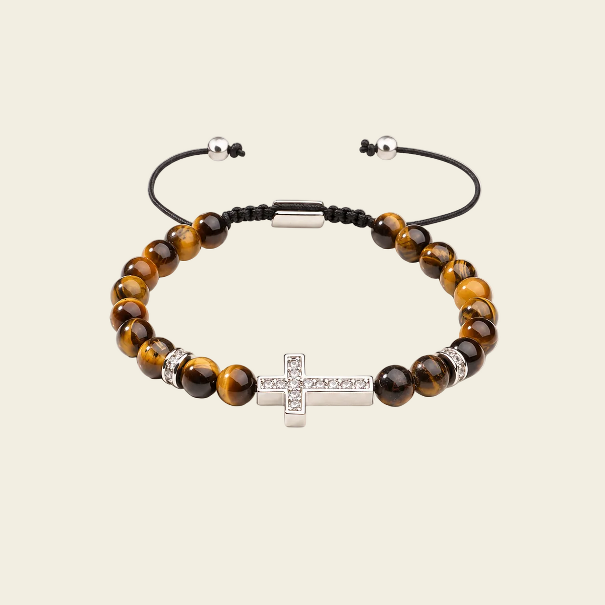 A beaded bracelet with brown and black tiger's eye beads, a silver-toned cross charm set with small clear stones, and an adjustable black cord closure on a light beige background.