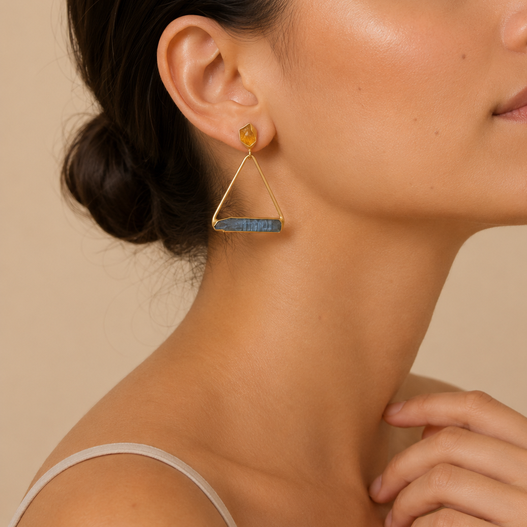 Woman wearing a gold earring with a gemstone on a beige background