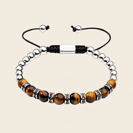 A beaded bracelet featuring polished brown tiger's eye beads, silver metallic spacer beads, a black adjustable cord, and a central silver rectangular clasp, displayed on a light beige background.