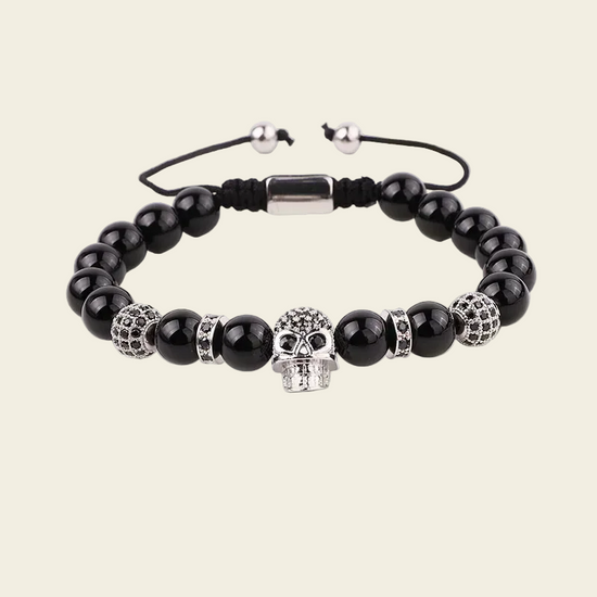 A beaded stretch bracelet featuring glossy black round beads, silver skull-shaped beads, textured silver spacer beads, and a black adjustable cord with silver metal beads.