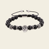 A beaded stretch bracelet featuring glossy black round beads, silver skull-shaped beads, textured silver spacer beads, and a black adjustable cord with silver metal beads.