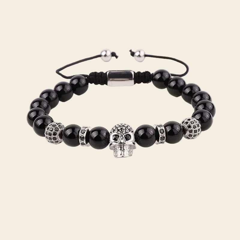 A beaded stretch bracelet featuring glossy black round beads, silver skull-shaped beads, textured silver spacer beads, and a black adjustable cord with silver metal beads.