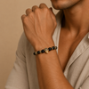 Person wearing a bracelet with black beads and gold accents on a beige background
