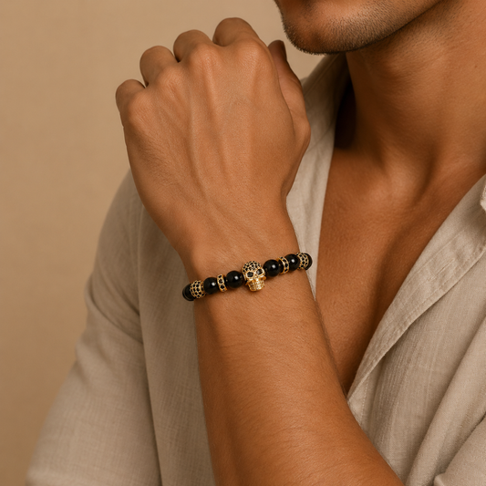 Person wearing a bracelet with black beads and gold accents on a beige background