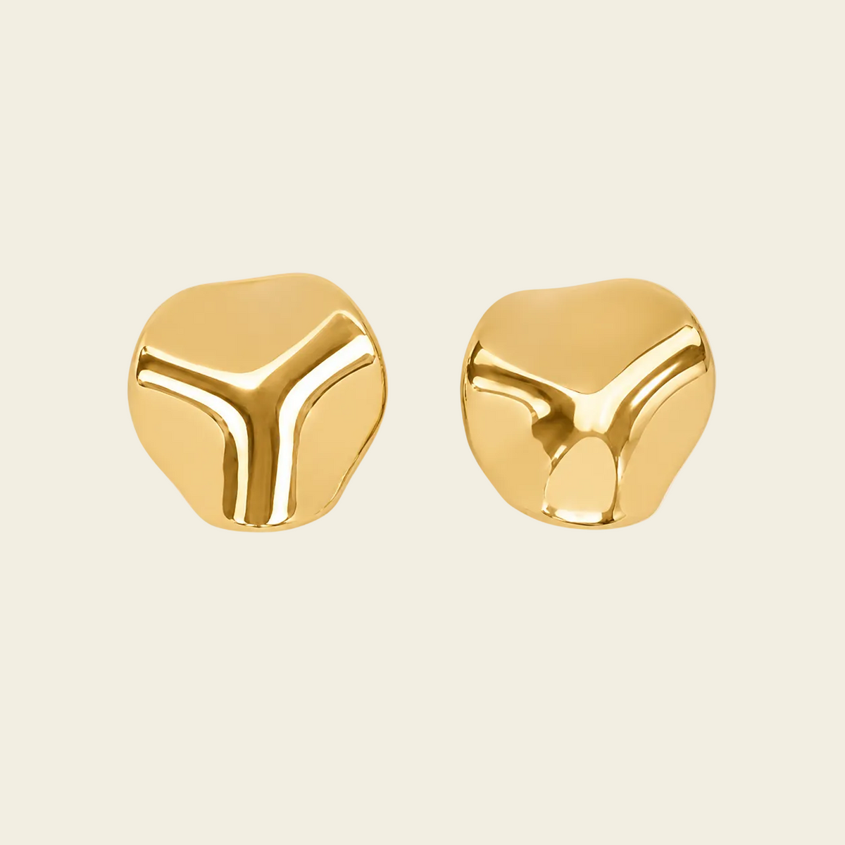 A pair of gold-colored, abstract three-dimensional stud earrings with a polished, reflective finish, displayed on a solid light beige background.