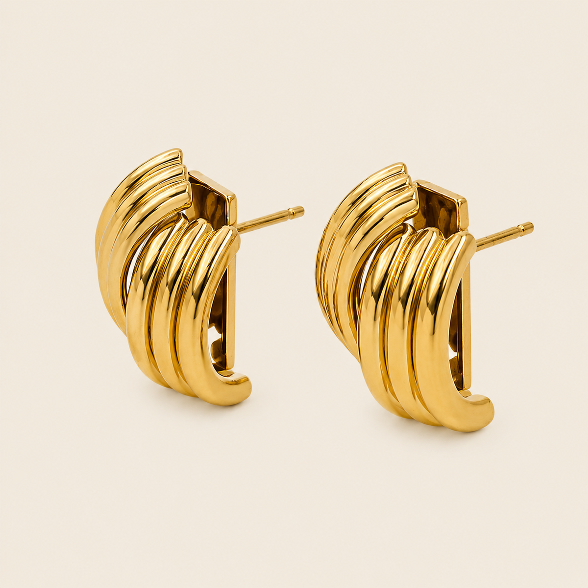 A pair of gold-toned hoop earrings with a layered, curved design, shown on a light beige background.