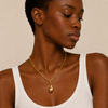Woman wearing a gold chain necklace with a pendant on a beige background
