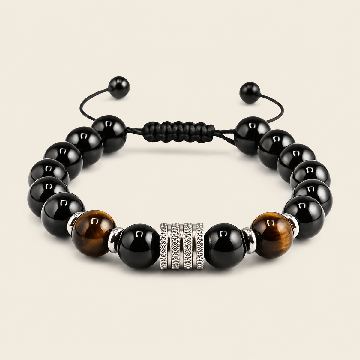A beaded stretch bracelet featuring glossy black round beads, two brown tiger's eye beads, a textured silver spacer, and a black adjustable cord closure, shown on a light beige background.