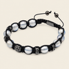 A black macrame bracelet featuring white freshwater pearls, silver-toned spacer beads, and an adjustable sliding closure, displayed on a light beige background.