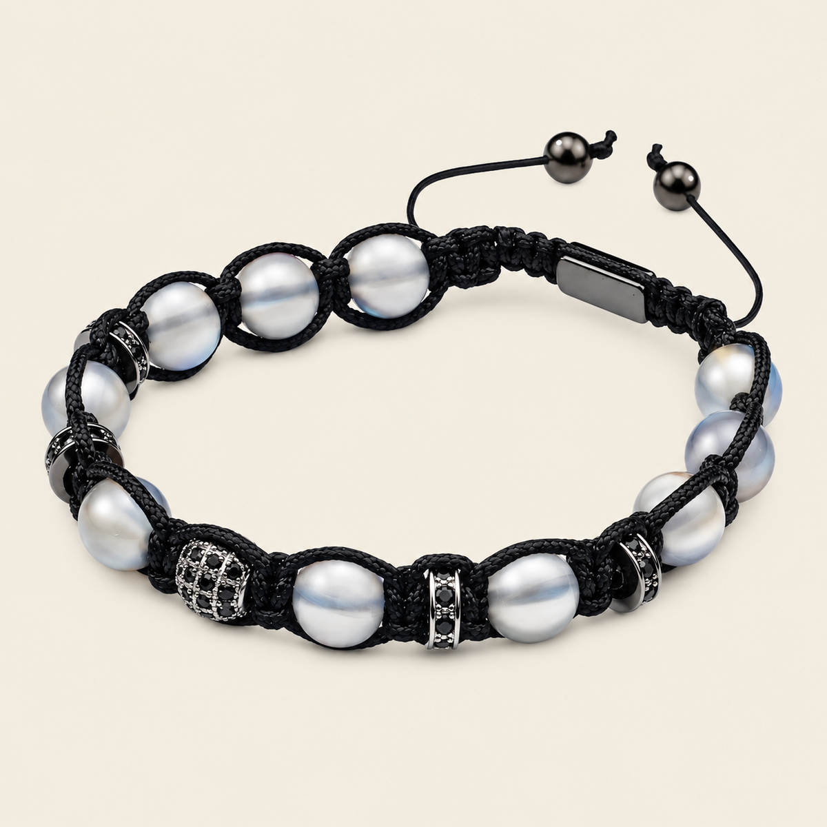 A black macrame bracelet featuring white freshwater pearls, silver-toned spacer beads, and an adjustable sliding closure, displayed on a light beige background.