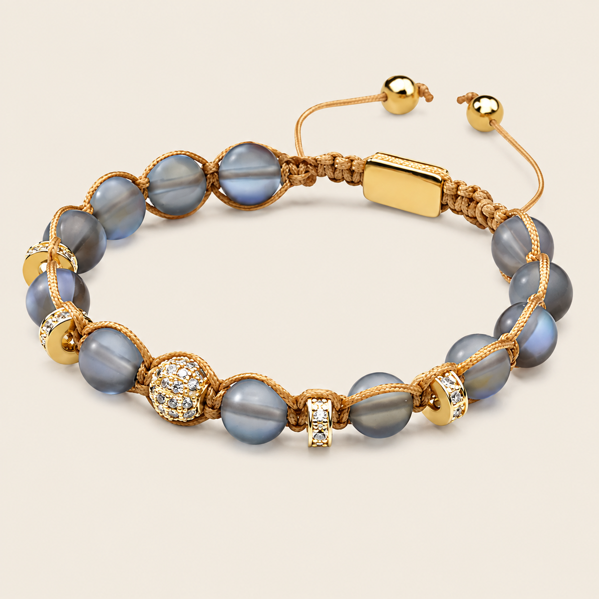 A gold-plated beaded bracelet with round blue-gray beads, gold spacer beads, and a gold magnetic clasp, displayed on a light beige background.