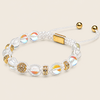 A beaded adjustable bracelet with clear round beads, iridescent beads, gold-toned spacer details, and a gold clasp on a white cord, shown on a light beige background.