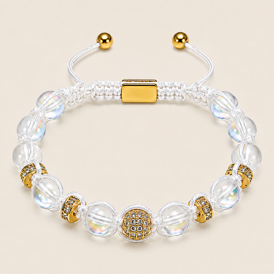 A white macrame bracelet with iridescent clear beads, gold spacer beads, and a central gold-plated square clasp, shown on a light beige background.