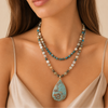 Woman wearing a beaded necklace with a large turquoise pendant on a beige background