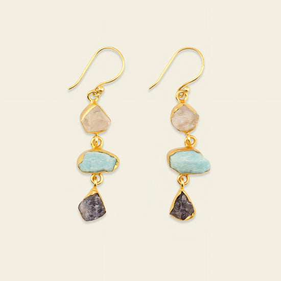 Pair of gold earrings with stone drops on a beige background