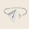 A polished silver-tone open cuff bangle bracelet with two triangular pyramid-like geometric elements, shown on a solid light beige background.